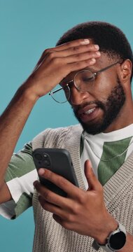 Phone, black man and stress in studio for fraud, pyramid scheme investment and phishing email. Person, technology and frustrated on blue background with failed payment, network error or banking scam