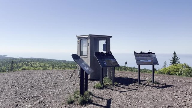 Camera pans past interpretive panels and a small booth at Brockway Mountain Overlook in Michigan above forested hills and a broad expanse of water.
