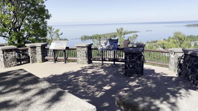 The camera approaches a stone and metal viewing platform on Brockway Mountain above Copper Harbor Michigan with interpretive panels a visitor and views of Lake Superior and Lake Fanny Hooe.