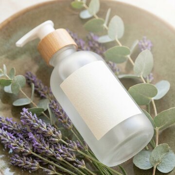 White cosmetic lotion pump bottle mockup with green eucalyptus leaves on soft background
