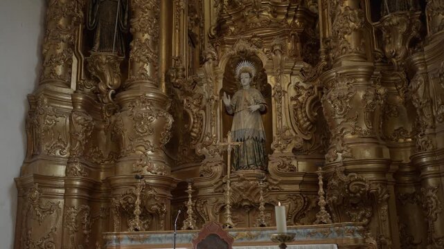 Painted statue of a saint in a niche of a carved and gilded altarpiece in the Tibaes monastery church near Braga, Portugal, a lit candle and cross on the altar.