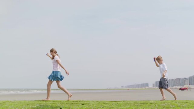 Girl and boy walking barefoot with kites on green algae shore side view tilt camera movement