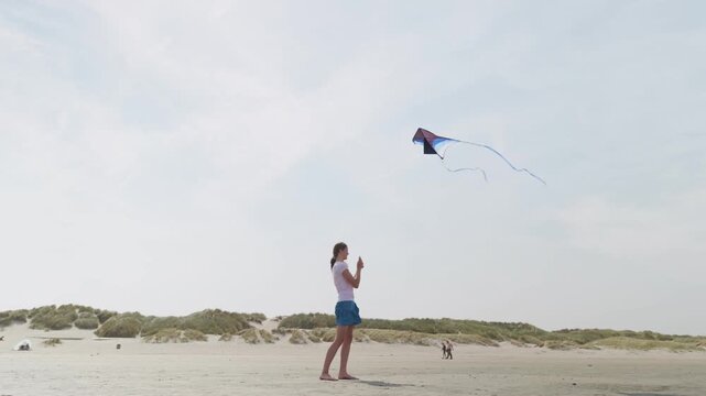 Girl flying a blue kite at a sandy beach slow motion sand dunes and the blue sky
