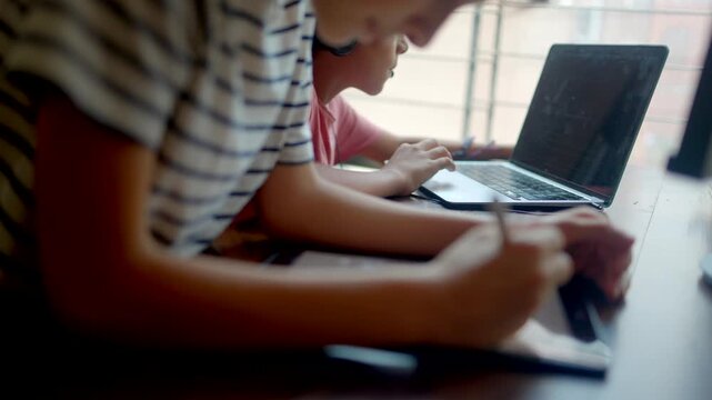 Focused kids studying online with laptop and graphic tablet at home desk, showcasing remote education, digital learning, and the future of online schooling