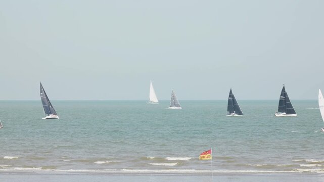 Sailing yachts offshore with a lifeguard flag in the foreground slow motion view from the beach