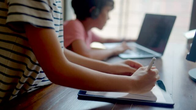 Children studying online from home using laptop and tablet for distance education, two kids doing homework together, e-learning and remote school lesson concept