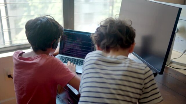 Young boys coding on a laptop computer with a second monitor, representing early stem education, future programmers, and remote online learning from home in quarantine
