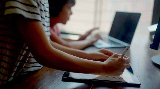 Two children studying at home using laptop and tablet, concept of homeschooling, online education, homework, e-learning, and new normal lifestyle during social distancing