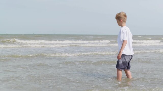 A fully clothed boy is standing in the sea kneeling in the water