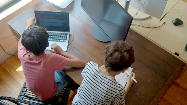 Two boys learning from home, one programming on a laptop and the other drawing on a tablet, showcasing modern education, technology, and creativity during remote school