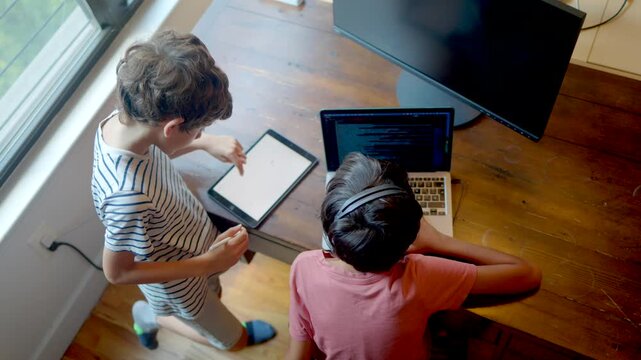 High angle view of two young boys using a laptop and a digital tablet for e-learning and entertainment, showcasing modern childhood and digital literacy at home