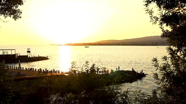 Sunset casts warm hues over water as boats move smoothly, framed by distant hills and lush vegetation, capturing a tranquil coastal atmosphere