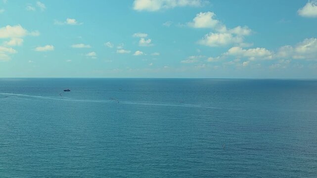 Small fishing boat moves across tranquil blue waters near rocky coastline with distant mountains under a clear sky, showcasing serene natural beauty and coastal scenery