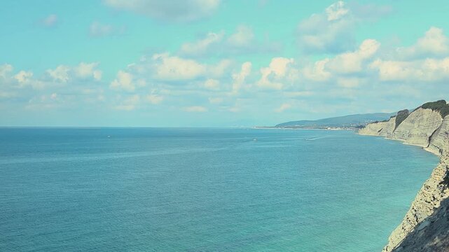 Small fishing boat moves across tranquil blue waters near rocky coastline with distant mountains under a clear sky, showcasing serene natural beauty and coastal scenery