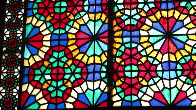 Vibrant stained glass windows with intricate Persian Orosi latticework and geometric patterns inside the historic Dowlatabad Garden pavilion in Yazd, Iran, showcasing traditional Iranian architecture.