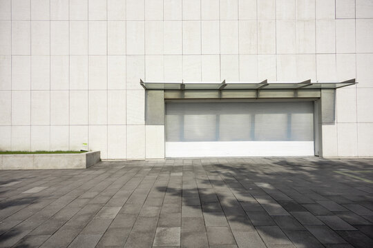 modern building white roller shutter door and gray paved ground with shadows