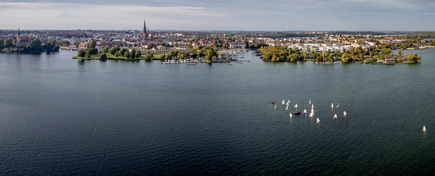 Panoramic aerial view of Lake Schwerin and city skyline with sailing boats, Germany. View of historic old town, cathedral spire, marina, waterfront architecture and group of white sailboats.