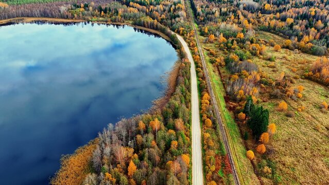 Aerial view of a winding road beside a reflective lake surrounded by colorful autumn foliage