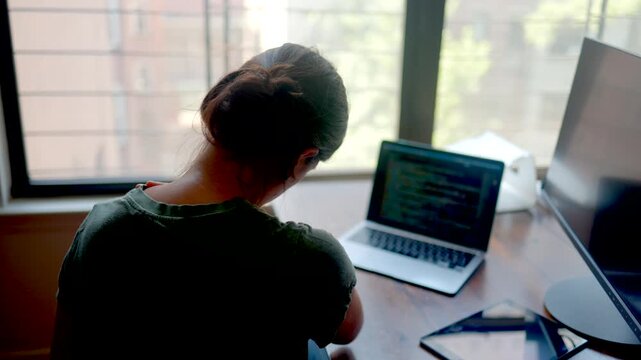 Overworked programmer experiencing neck pain and fatigue while coding on a laptop, a female developer massaging her sore shoulder due to sedentary work and burnout