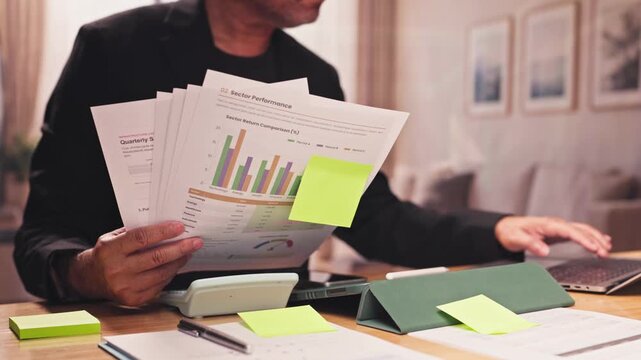 Businessman analyzes sector performance charts, papers, laptop desk at home. Financial investment audit, corporate market research analysis, quarterly revenue report review.