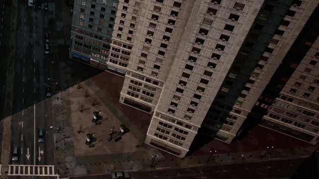 High angle view of city skyscrapers casting sharp morning shadows over a busy street corner with cars driving in clear daylight.
