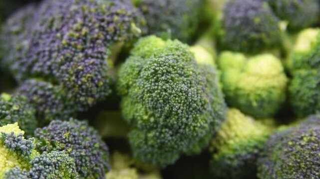 Close up view of raw fresh green broccoli florets in metal bowl and on wooden table surface background prepared for healthy vegan cooking.