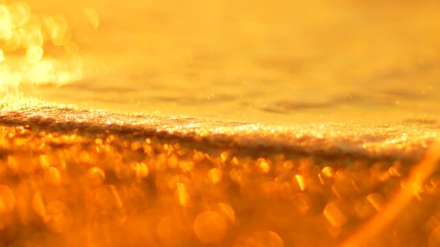 Warm sunlight glowing on wet sand as gentle ocean waves wash ashore during sunset. Macro close up shot.