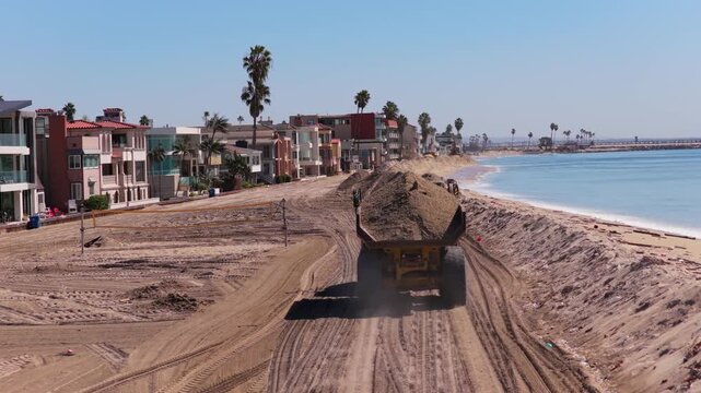 Long Beach, California, USA - October 15, 2026: Dump truck hauls sand along a berm raising the beach to protect oceanfront homes from flooding after Tropical Storm Rachel, Alamitos Bay jetty ahead.