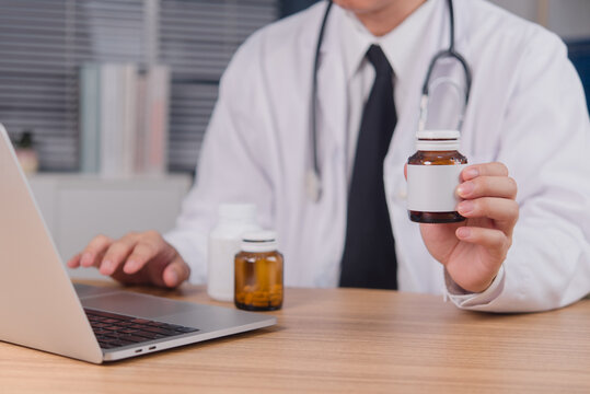 Doctor holding medicine bottle and working on laptop at desk