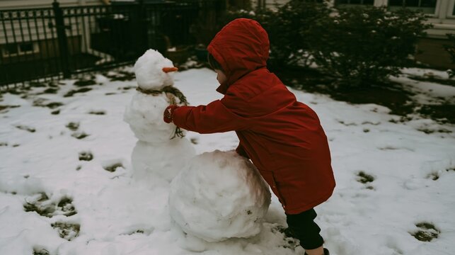 Child in a bright red coat building a snowman during winter outdoor
