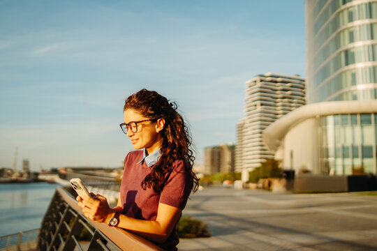 Woman checking smartphone during golden hour in modern city