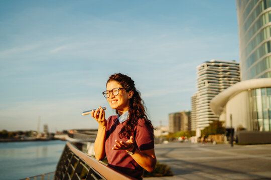 Woman recording voice message on smartphone in city