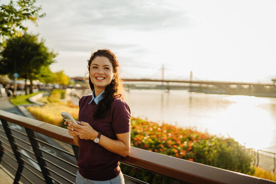 Woman smiling using phone along belgrade river at sunset