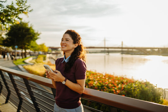 Woman smiling using smartphone river promenade sunset