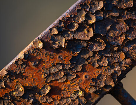 Close-up view of a severely weathered metal surface featuring thick layers of dark peeling paint and orange oxidation texture