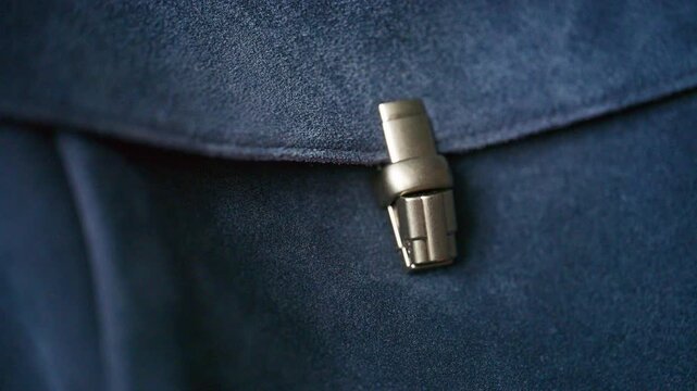 Stylish navy suede crossbody bag with flap closure secured by metallic clasp, worn against brown trousers and belt.
