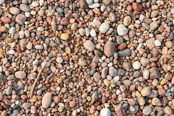 Nature background featuring smooth river stones, small pebbles, and a twig on the ground © Indre