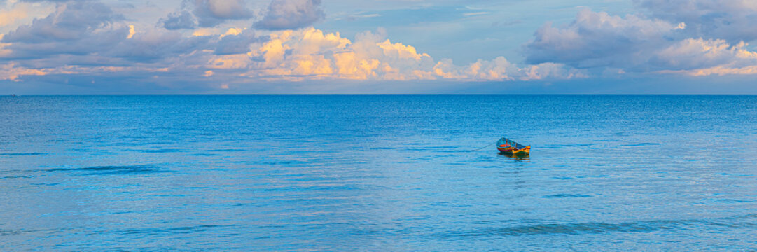 Waves softly lap against a small boat floating in the blue water under a cloudy sky near the shore