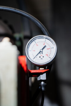 Analog pressure gauge with bar and MPa scales connected to a hose and lever valve, showing instrumentation used for pressure measurement in industrial fluid system servicing