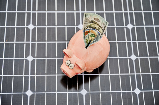 Piggy bank with dollar bill on solar panel top view. Concept of saving money, financial return and investment in renewable energy and electricity