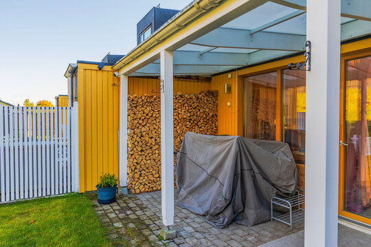 Beautiful view of patio with furniture covered for winter and firewood stacked beside wooden house. Sweden.