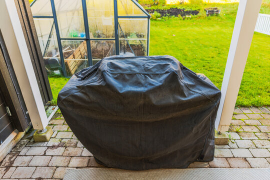 Close-up view of barbecue grill with protective cover on paved patio in autumn. Sweden.