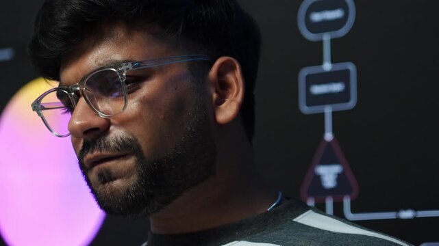Indian male developer speaking and gesturing during project meeting in a dark studio, with a glowing flowchart diagram, AI training software development