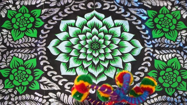 Traditional floral mandala pattern in green and silver color on a dark background texture.