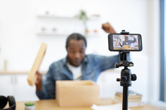 A creator films a hands-on cardboard box demonstration in a bright workspace, using a smartphone mounted on a tripod to capture the process