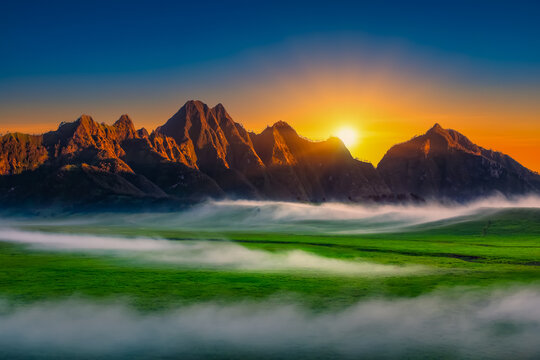 Ein Landschaftsbild mit Vulkankette, Wiese unten mit einer Nebelschwade und Sonnenaufgang