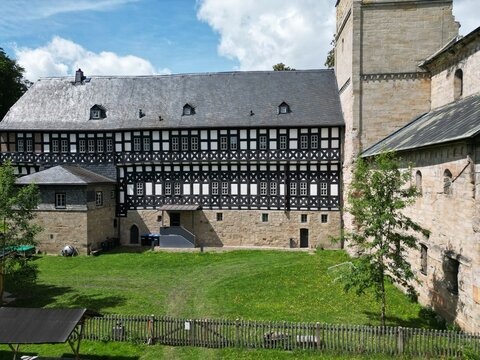 Half-timbered half-timbered building with a grey slate roof beside the Romanesque tower of Paulinzella Abbey on a sunny summer day, Thuringia, Germany