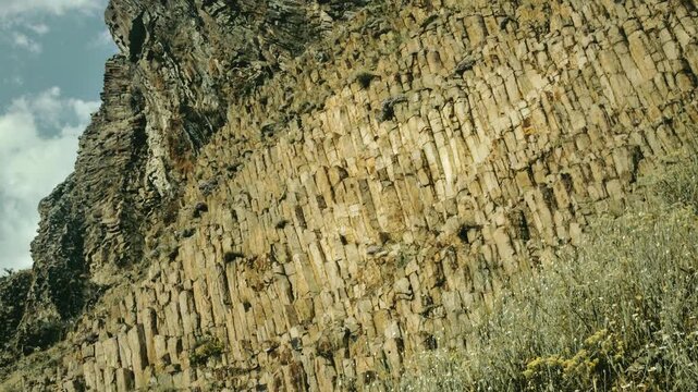 Columnar basalt cliff formation in Guvem valley with green hills and cloudy sky, Kizilcahamam, Ankara, Turkey