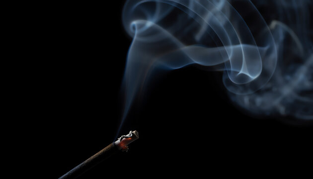 Thin smoke curls upward from a burning incense stick against a pitch-black background, creating a serene and mysterious atmosphere.