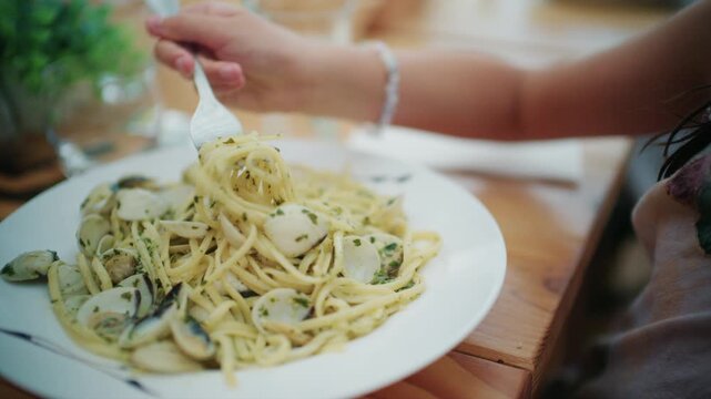 Close-up of spaghetti with clams, garlic and parsley on a white plate as a girl twirls pasta onto her fork, French Riviera, France.